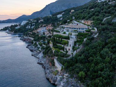Uçurumun kenarına kurulmuş geniş, lüks bir villanın geniş manzarası. Deniz manzaralı, yemyeşil bahçeler ve çevreleyen doğa tarafından tamamlanmış..