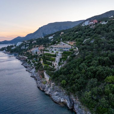 Yamaç manzaralı bir villa kompleksi. Yeşillik ve kayalık sahil karışımı. Sakin sular ve alacakaranlığın yumuşak renkleri manzarayı güzelleştirir..