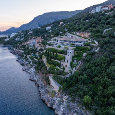 Havadan bakıldığında kayalık bir yamaçta geniş bir sahil arazisi, karmaşık bir mimari ve yemyeşil bitki örtüsü sergileniyor. Aşağısı sakin.  