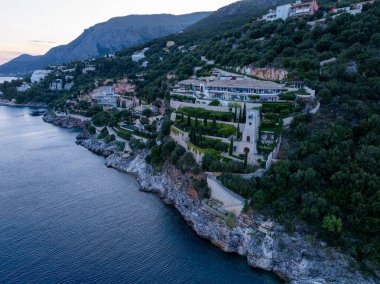 Sersemletici bir malikane kayalık bir kayalık yamaçtan aşağı süzülüyor sakin bir denize bakan, yemyeşil ve uzak dağlık arazide yuva yapmış..