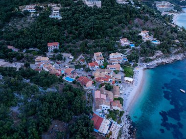 Canlı ağaçlarla çevrili, deniz kenarındaki büyüleyici bir köyün havadan görünüşü ve berrak turkuaz suları olan el değmemiş bir plaj..