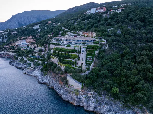 Manzaralı bir manzara, mavi okyanusa bakan yemyeşil bir yamaçtaki büyük bir konutu yakalar. Mimaride teraslar var..