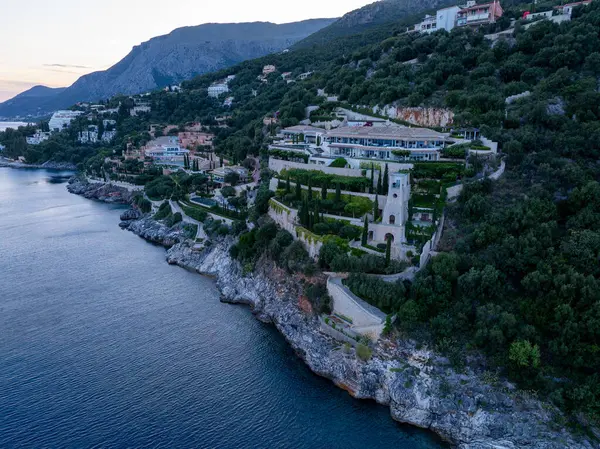 Sersemletici bir malikane kayalık bir kayalık yamaçtan aşağı süzülüyor sakin bir denize bakan, yemyeşil ve uzak dağlık arazide yuva yapmış..