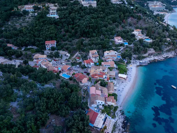 Canlı ağaçlarla çevrili, deniz kenarındaki büyüleyici bir köyün havadan görünüşü ve berrak turkuaz suları olan el değmemiş bir plaj..