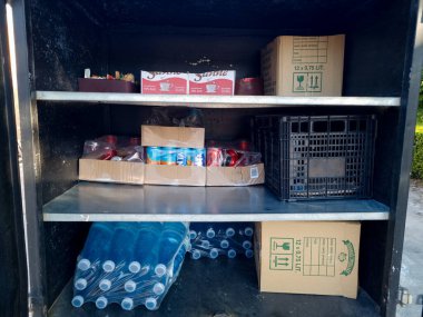 Açık hava ortamındaki karanlık bir deponun raflarında çeşitli içecekler, atıştırmalıklar ve diğer ihtiyaçlar düzenlenir..