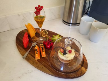 Tropikal meyveler, tutkulu meyve suyu ve mermer bir yüzey üzerinde sergilenen kremalı lezzetli bir hamur işi içeren sanatsal olarak düzenlenmiş bir tabak..