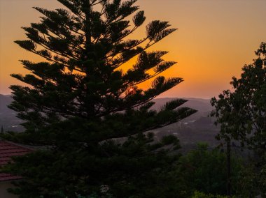 Gün batımında manzaraya gölge düşüren uzun ağaç kuleleri. Güneş uzak dağların ve renkli gökyüzünün üzerinde batar..