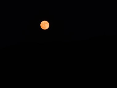Minimalist bir fotoğrafta yer alan turuncu bir gök küresi karanlık gece gökyüzünde parıldıyor. Karanlık kürenin etrafını sarar ve kontrast ekler..