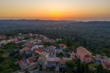 Şafakta küçük bir Avrupa köyünün manzarası. Etrafı bereketli ormanlar ve yuvarlanan tepelerle çevrili. Önünde pembe bir kilise var..