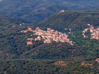 Yoğun bir tepe bölgesindeki sık ağaçların arasında yer alan bir köyün manzarası. Bu köy kırmızı kiremit çatılı evlerle dolu..