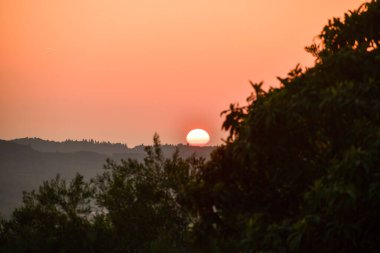Sisli dağların üzerinde büyüleyici bir gün doğumu. Yumuşak turuncu gökyüzü, sakin, doğa dolu bir sabah manzarası için sahneyi hazırlıyor.. 
