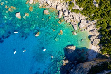 Gizli bir taşın tepeden aşağı havadan görüntüsü: kristal berrak turkuaz suyu ve Yunanistan 'ın Korfu kenti yakınlarındaki tekneleri olan tenha bir cennet plajı. Dokunulmamış doğal bir kıyı manzarası.