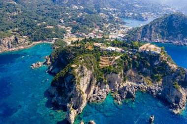 Yunanistan 'ın Korfu kentindeki Paleokastritsa kıyı şeridinin nefes kesici manzarası. Bereketli yeşil kayalıklar İyon Denizi 'nin büyüleyici turkuaz ve derin mavi sularıyla karşılaşıyor, aşağıdaki plajlar ve köylerle.