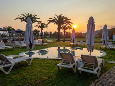 Siluetli palmiye ağaçları olan tropikal bir tatil köyünde canlı bir HDR gündoğumu. Altın güneş, dinlendirici bir tatil sabahı için dinlenme yerleriyle çevrili sakin yüzme havuzunda mükemmel bir şekilde yansıyor.