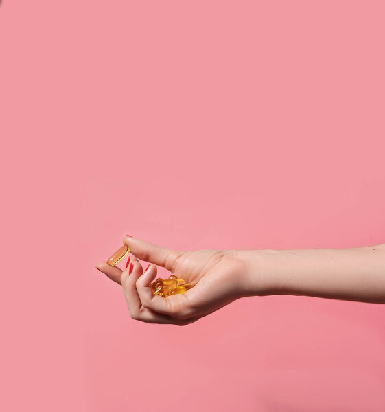 Женская рука держит много капсул масла на розовом фоне. Концепция благополучия