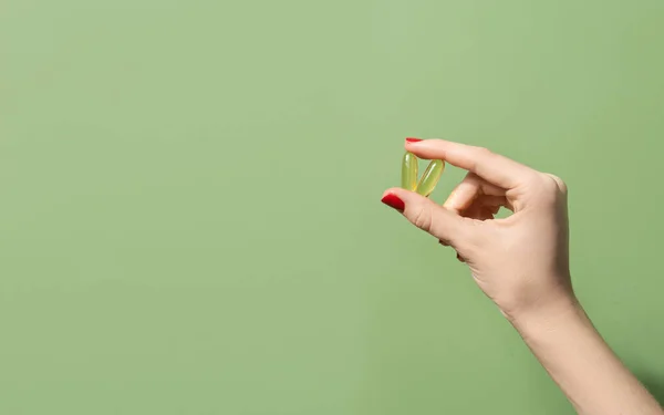 stock image Female hand holding two oil capsules on green background. Wellbeing concept