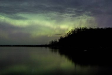 Kuzey ışıkları, parçalı bulutlu bir gecede kuzey Michigan 'daki kara nehrin ağzına yansıyor..