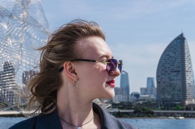 Güneş gözlüklü genç bayan dik duruyor.