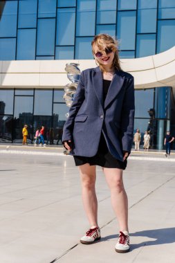Takım elbiseli ve güneş gözlüklü beyaz bir kadının dikey fotoğrafı.