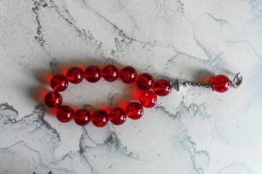 Açık mermer bir yüzey üzerinde oval bir şekilde dizilmiş büyük, parlak kırmızı dua boncukları..