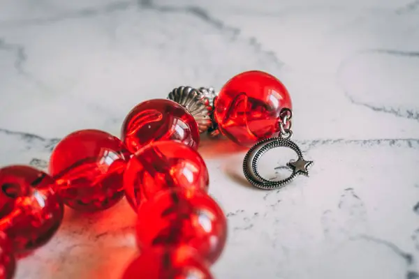 Açık mermer bir yüzey üzerinde oval bir şekilde dizilmiş büyük, parlak kırmızı dua boncukları..