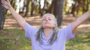 Sağlıklı, orta yaşlı, gri saçlı bir kadın parkta yoga yapıyor.