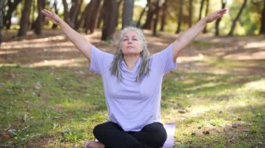 Sağlıklı, orta yaşlı, gri saçlı bir kadın parkta yoga yapıyor.