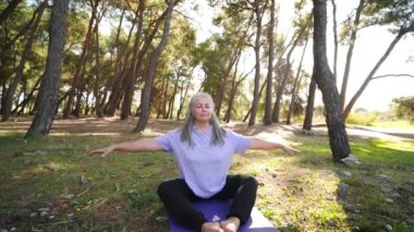 Sağlıklı, orta yaşlı, gri saçlı bir kadın parkta yoga yapıyor.