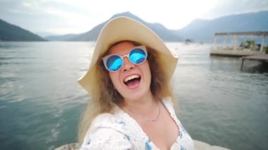 Kameraya gülümseyen şapkalı genç kadın özgürlüğün tadını çıkaran gezgin kadın dağda gün batımında selfie çekiyor.
