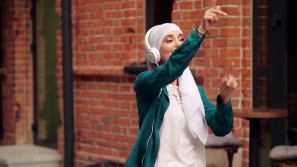 ヘッドフォンで音楽を聞き 屋外で踊るヒジャーブの中東の女性 女性の自立とフェミニズムの概念 — ストック動画