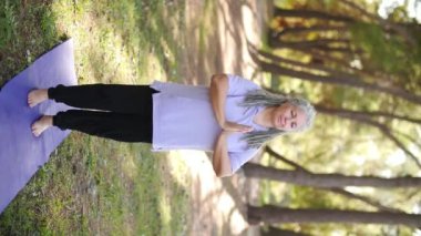 Sağlıklı, orta yaşlı, gri saçlı bir kadın parkta yoga yapıyor.