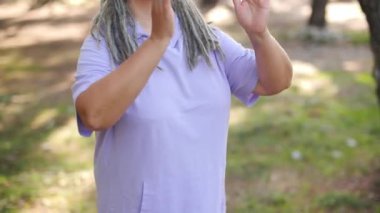 Sağlıklı, orta yaşlı, gri saçlı bir kadın parkta yoga yapıyor.