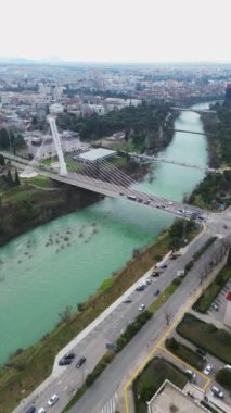 Tatil ve seyahat konsepti. Podgorica Karadağ: Moraca nehri ve tarihi eser olan Millennium köprüsü de dahil olmak üzere şehir merkezinin üzerindeki güzel günbatımı. Hava görünümü.