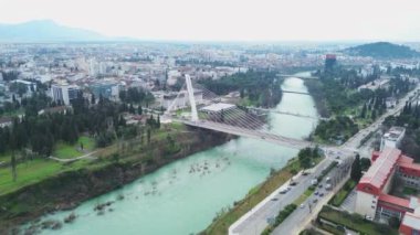 Tatil ve seyahat konsepti. Podgorica Karadağ: Moraca nehri ve tarihi eser olan Millennium köprüsü de dahil olmak üzere şehir merkezinin üzerindeki güzel günbatımı. Hava görünümü.