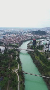 Tatil ve seyahat konsepti. Podgorica Karadağ: Moraca nehri ve tarihi eser olan Millennium köprüsü de dahil olmak üzere şehir merkezinin üzerindeki güzel günbatımı. Hava görünümü.