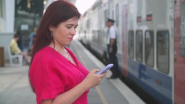 Tren gelene kadar akıllı telefon kullanan bir kadın. İleti iletileri e- posta ya da tren tarifesi kontrol ediliyor
