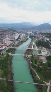 Tatil ve seyahat konsepti. Podgorica Karadağ: Moraca nehri ve tarihi eser olan Millennium köprüsü de dahil olmak üzere şehir merkezinin üzerindeki güzel günbatımı. Hava görünümü.