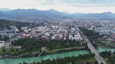 Tatil ve seyahat konsepti. Podgorica Karadağ: Moraca nehri ve tarihi eser olan Millennium köprüsü de dahil olmak üzere şehir merkezinin üzerindeki güzel günbatımı. Hava görünümü.