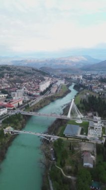 Tatil ve seyahat konsepti. Podgorica Karadağ: Moraca nehri ve tarihi eser olan Millennium köprüsü de dahil olmak üzere şehir merkezinin üzerindeki güzel günbatımı. Hava görünümü.