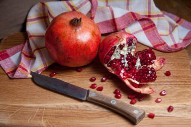 Olgun kırmızı nar ve çatlamış nar bileşimi. Ahşap bir arka planda klasik bıçakla. Yakut tohumlarının yakın görüntüsü nar meyvesi