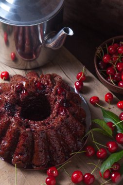 Koyu renk ahşap arka planda kompozisyon - tatlı kirazlı lezzetli çikolatalı pasta, eski moda çaydanlık, kiraz meyveli kiraz kasesi ve kiraz ağacı yapraklı kiraz.