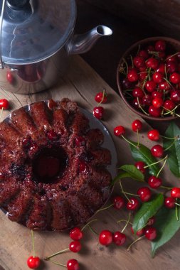 Koyu renk ahşap arka planda kompozisyon - tatlı kirazlı lezzetli çikolatalı pasta, eski moda çaydanlık, kiraz meyveli kiraz kasesi ve kiraz ağacı yapraklı kiraz.