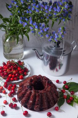 Beyaz arkaplanda kompozisyon - tatlı kirazlı lezzetli çikolatalı pasta, kirazlı beyaz tabak, kaliteli çaydanlık ve güzel mavi çiçekli cam kavanoz.