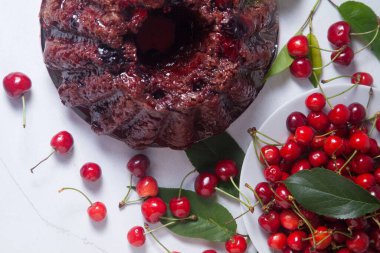 Tatlı kirazlı lezzetli çikolatalı pasta, beyaz tepside tatlı kiraz ve beyaz arka planda yeşil kiraz ağacı yaprakları.