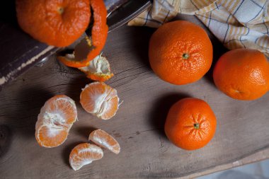 Soyulmamış taze portakal, mandalina, mandalina, mandalina, narenciye, meyvenin yarısı soyulmuş ve ahşap yaban domuzu üzerinde soyulmuş mandalina dilimleri.