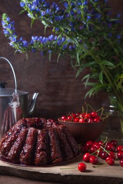 Koyu renk ahşap arka planda kompozisyon - tatlı kirazlı lezzetli çikolatalı pasta, kirazlı kirazlı kiraz kasesi, kaliteli çaydanlık ve güzel mavi çiçekli cam kavanoz.