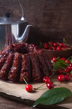 Koyu renk ahşap arka planda kompozisyon - tatlı kirazlı lezzetli çikolatalı pasta, eski moda çaydanlık, kiraz meyveli kiraz kasesi ve kiraz ağacı yapraklı kiraz.