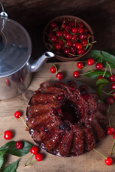 Koyu renk ahşap arka planda kompozisyon - tatlı kirazlı lezzetli çikolatalı pasta, eski moda çaydanlık, kiraz meyveli kiraz kasesi ve kiraz ağacı yapraklı kiraz.