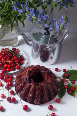 Beyaz arkaplanda kompozisyon - tatlı kirazlı lezzetli çikolatalı pasta, kirazlı beyaz tabak, kaliteli çaydanlık ve güzel mavi çiçekli cam kavanoz.