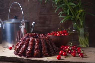 Koyu renk ahşap arka planda kompozisyon - tatlı kirazlı lezzetli çikolatalı pasta, kirazlı kirazlı kiraz kasesi, kaliteli çaydanlık ve güzel mavi çiçekli cam kavanoz.